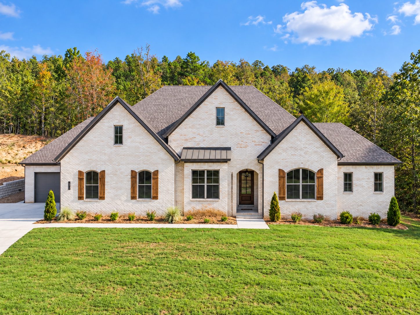 The front facade of 14600 Stonebrook Lane in Maumelle, Arkansas showcases a striking white brick contemporary home with multiple peaked rooflines and copper-trimmed windows set against a backdrop of mature autumn-toned trees.